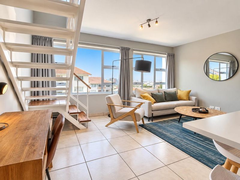 Bright open-plan living area featuring a modern staircase, large windows with city views, and neutral tiled flooring.