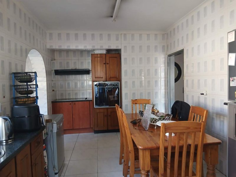 Open-plan kitchen and dining area featuring dated wall tiles, built-in wooden cabinetry, and a built-in oven.
