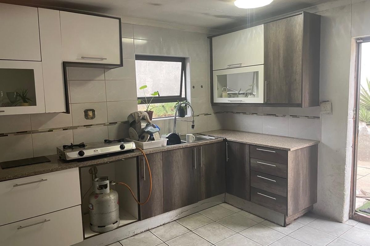 A compact kitchen featuring two-tone cabinetry, tiled splashbacks, and a gas hob, requiring some ceiling repairs and finishing touches.