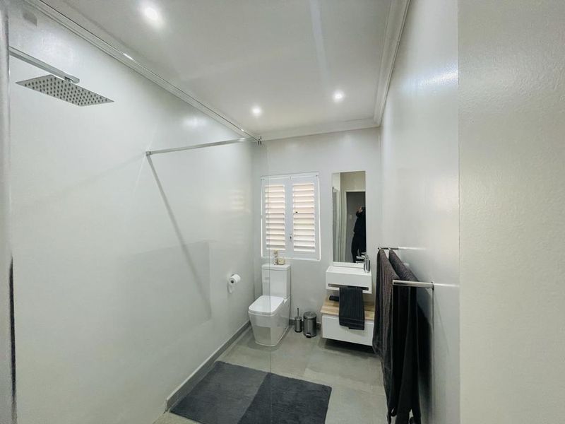 Modern bathroom featuring a walk-in shower with a rain shower head, wall-mounted vanity, and a toilet with shutter window blinds.