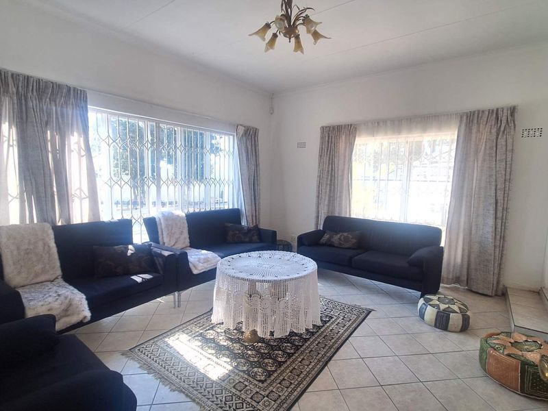 A spacious living room featuring tiled flooring and large windows fitted with security bars, offering a bright and functional living space.