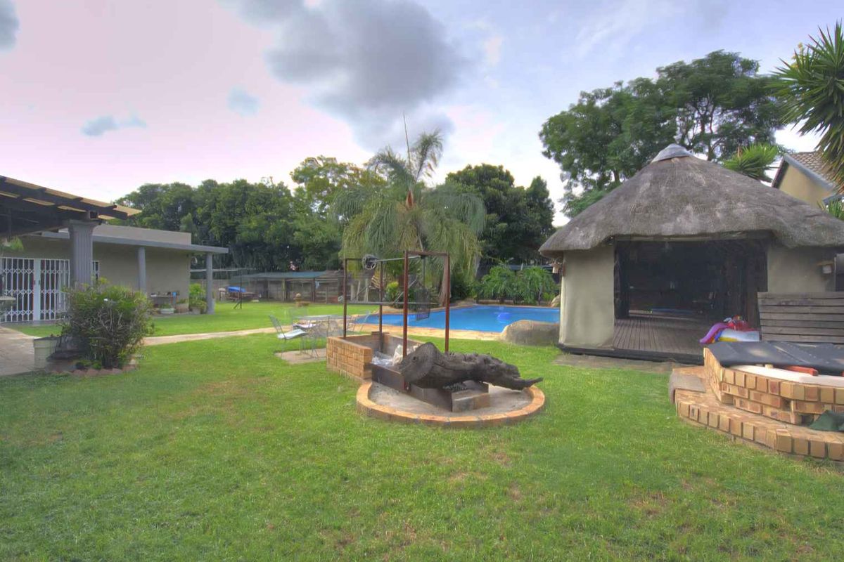 Spacious backyard featuring a swimming pool, a thatched lapa entertainment area, and a built-in brick braai facility set within a landscaped garden.