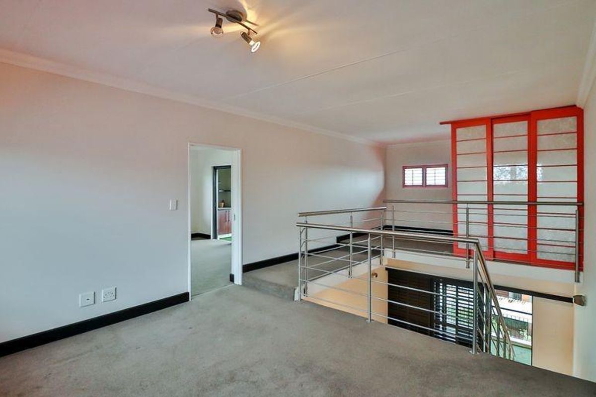 A mezzanine level living area featuring a stainless steel balustrade, carpeted flooring, and a distinctive red-framed sliding partition screen.