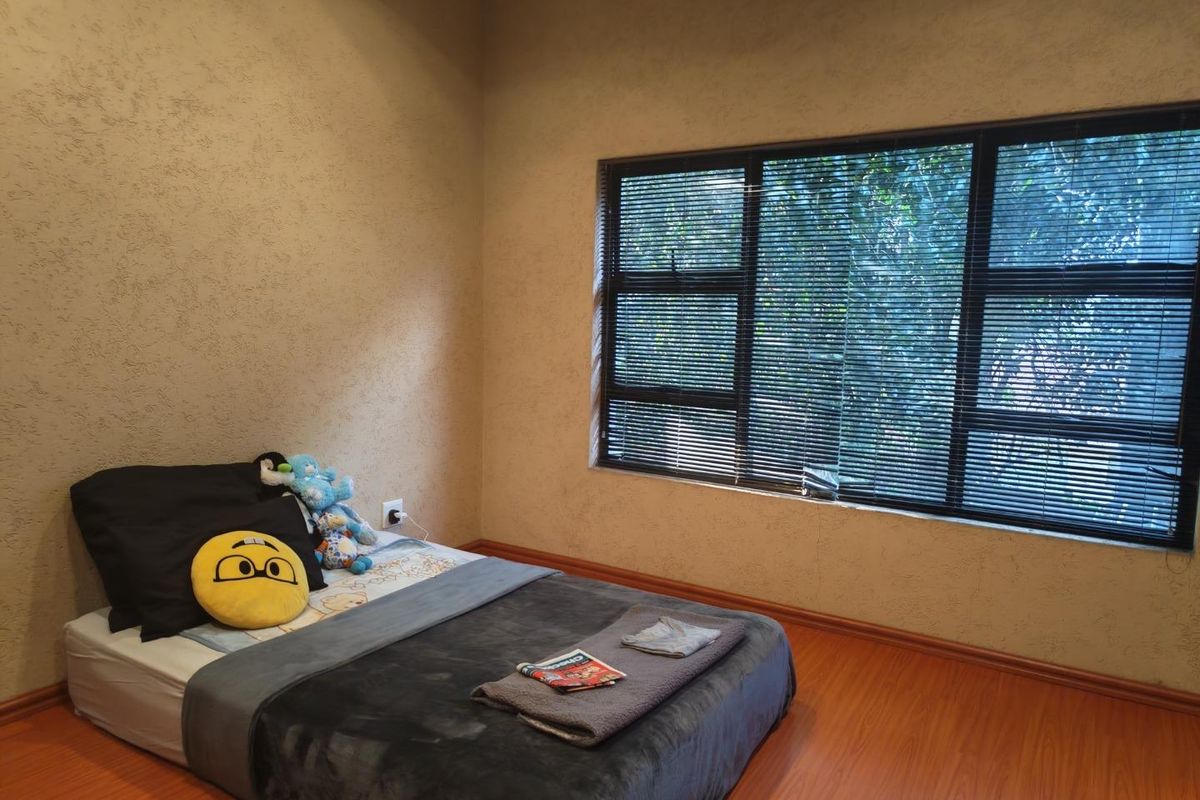 A bedroom featuring laminate flooring, textured walls, and large aluminium-framed windows fitted with venetian blinds.