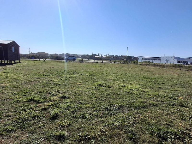 A wide, open vacant commercial land plot featuring a grass lawn and perimeter wire fencing, suitable for future development.