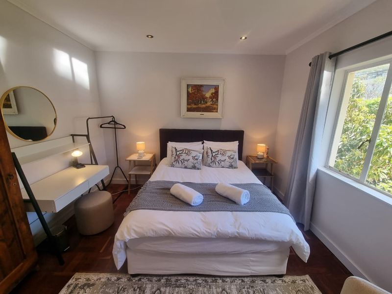A well-maintained bedroom featuring warm parquet flooring, recessed downlighting, and a large window allowing for natural light.