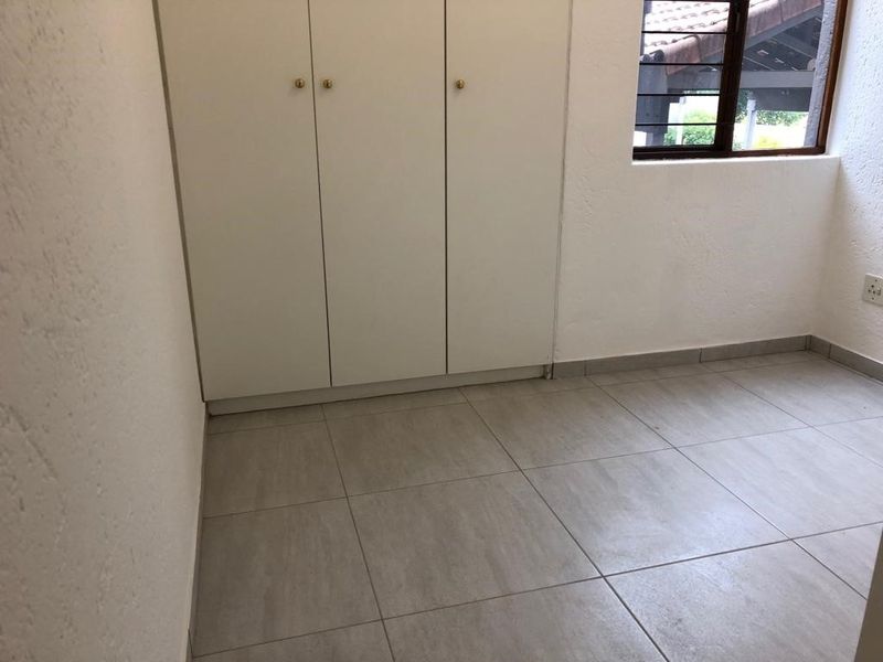A clean, empty bedroom featuring neutral tiled flooring, built-in cupboards, and a window with security bars, offering a blank canvas for personalization.