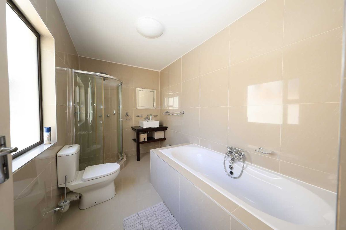 A clean, modern bathroom featuring a tiled bathtub, a separate glass-enclosed shower, a pedestal-style vanity, and a toilet.