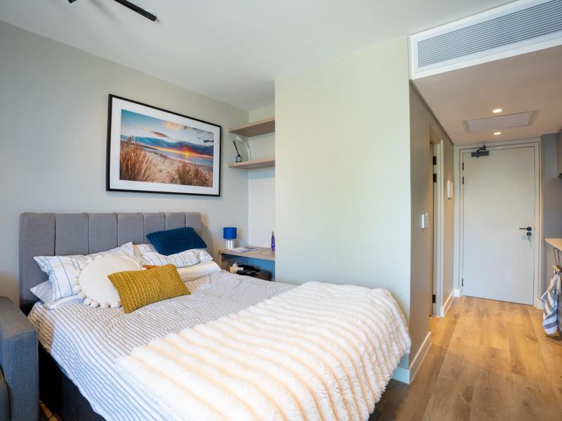 A modern open-plan studio apartment featuring a sleeping area with built-in shelving and a compact kitchen with integrated appliances and stone countertops.