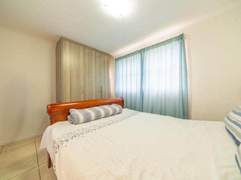 A functional bedroom featuring tiled flooring, neutral walls, and a built-in wardrobe with wood-grain finish cabinetry.