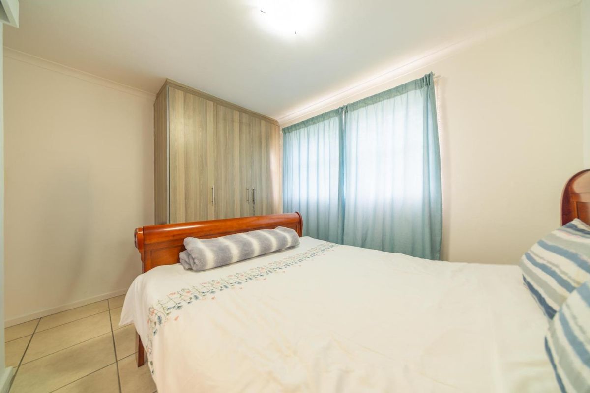A functional bedroom featuring tiled flooring, neutral walls, and a built-in wardrobe with wood-grain finish cabinetry.