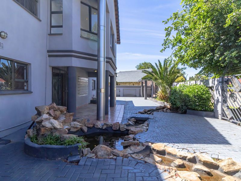 Rear exterior view featuring a paved driveway, a decorative rock water feature, and secure boundary walling with metal gate access.