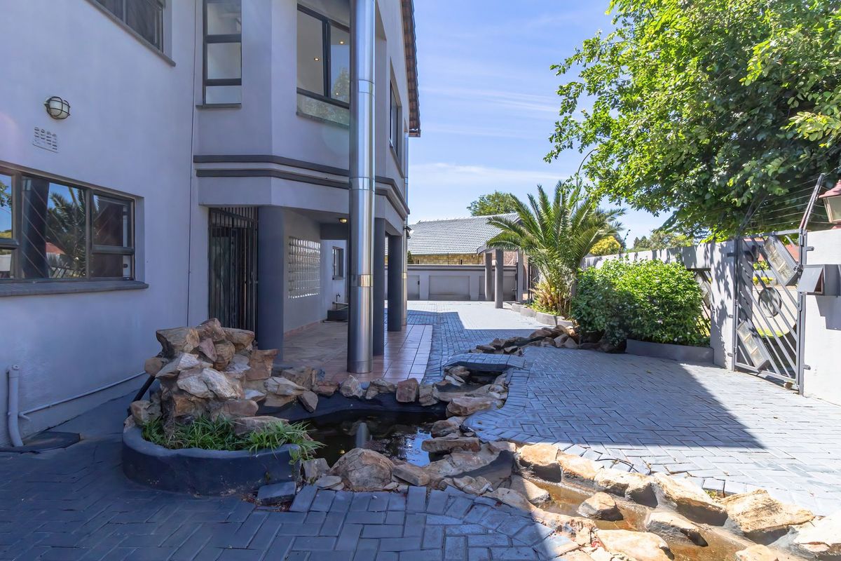 Rear exterior view featuring a paved driveway, a decorative rock water feature, and secure boundary walling with metal gate access.