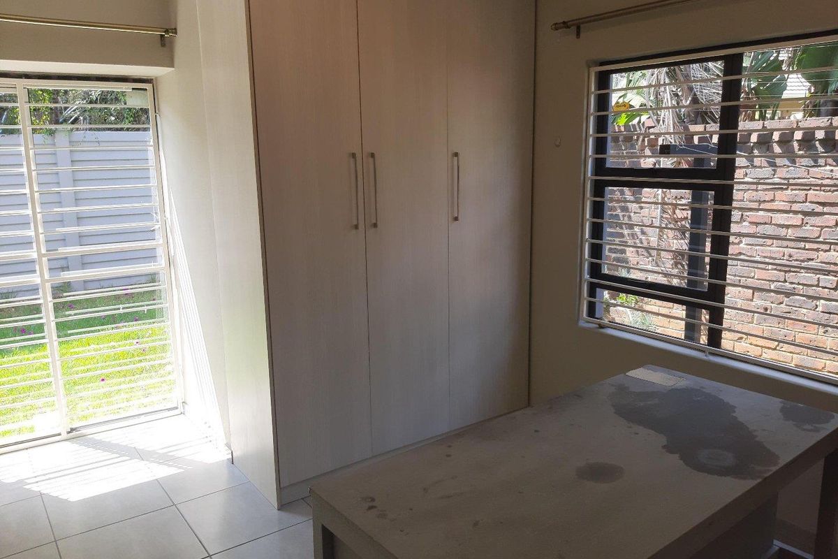A bedroom featuring built-in cupboards, tiled flooring, and a sliding door providing access to the garden area.