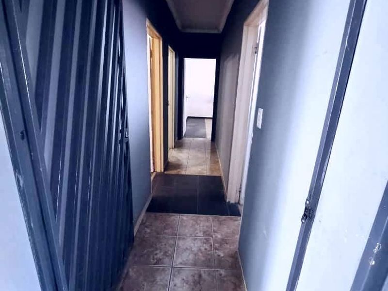 A narrow interior hallway featuring tiled flooring, a security gate, and decorative ceiling cornicing, providing access to multiple rooms.