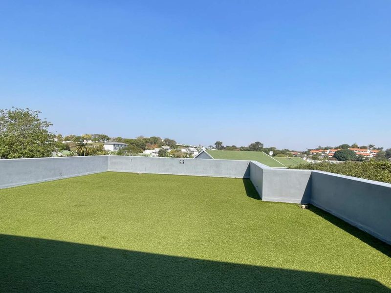 An open-air rooftop balcony featuring artificial turf flooring and a surrounding parapet wall, offering clear elevated views of the surrounding neighbourhood.