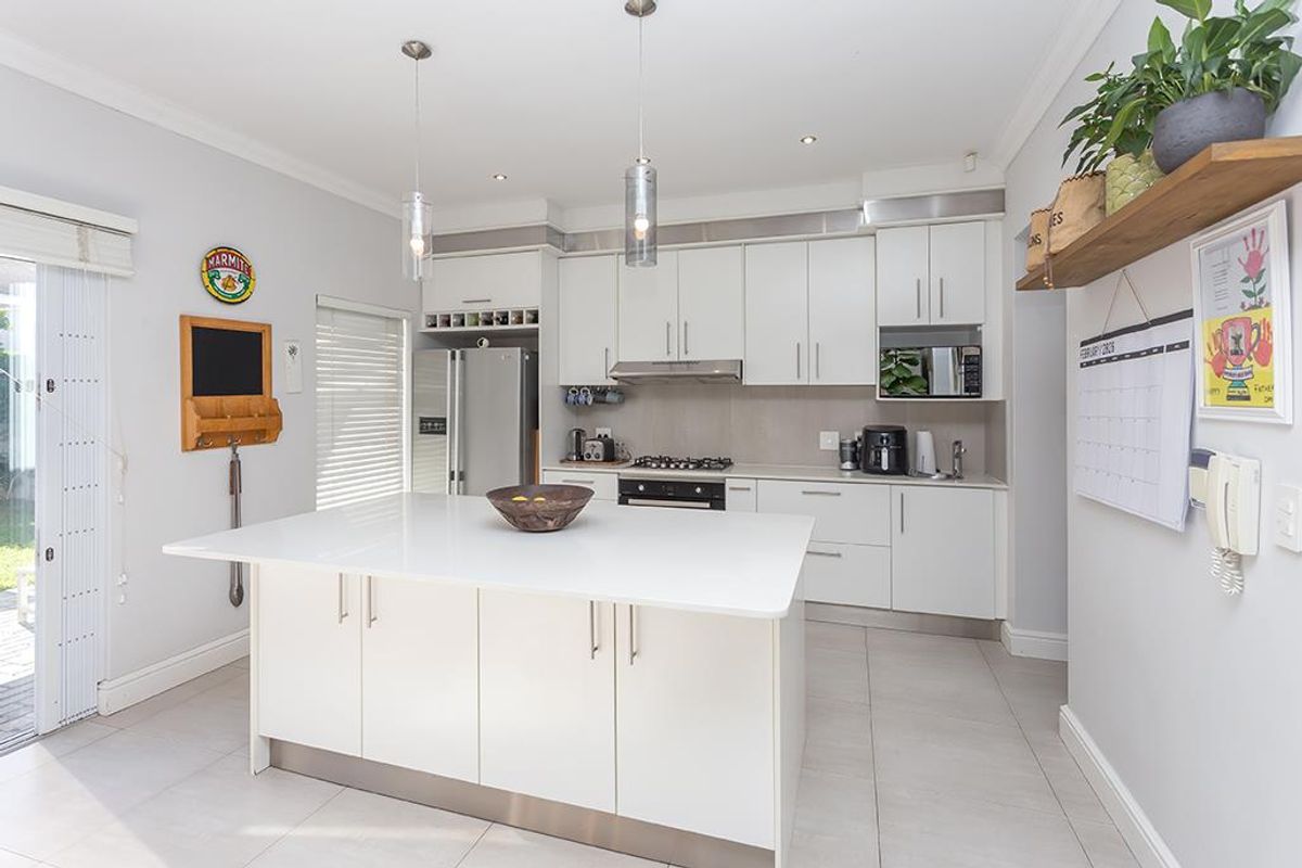 Modern kitchen featuring a central island, white cabinetry, stone countertops, gas hob, and integrated appliances, with direct access to the outdoor area.