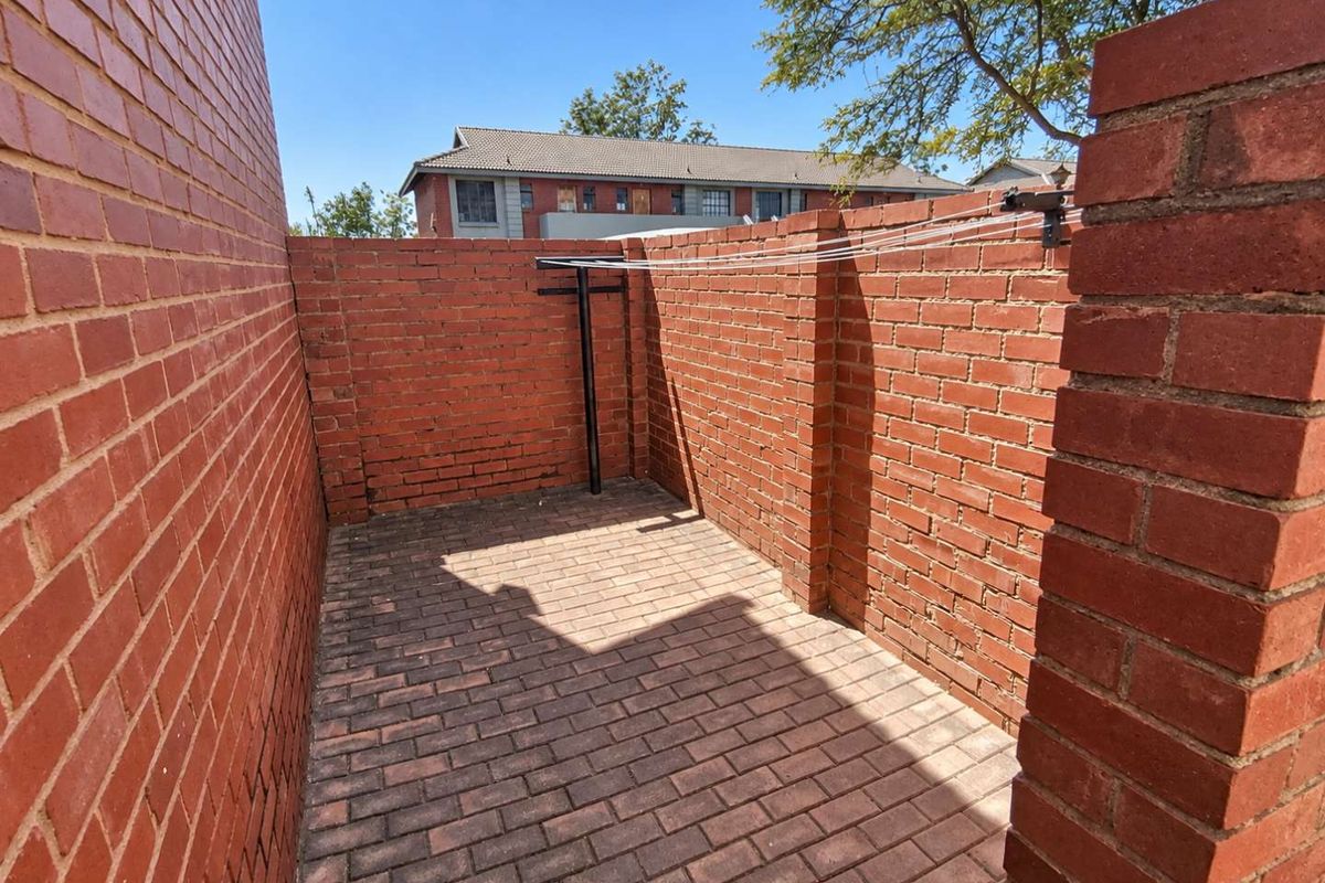 A private rear courtyard area featuring durable brick paving and high brick boundary walls, equipped with a fixed wall-mounted washing line.