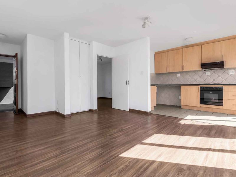 Open-plan living area featuring laminate flooring and a functional kitchen with built-in cabinetry, oven, and extractor fan.