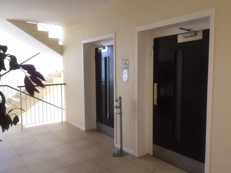 A clean apartment building hallway featuring elevator access and a staircase with a metal balustrade.