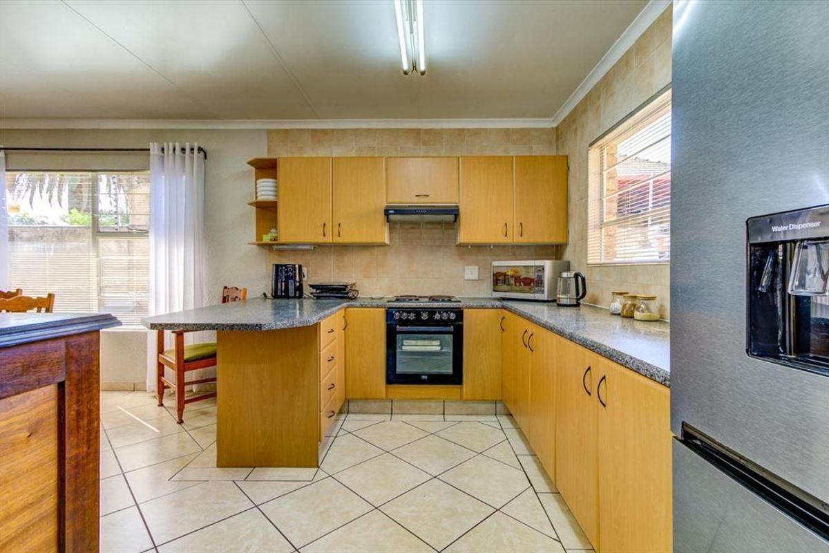 A functional kitchen featuring light wood cabinetry, granite-look laminate countertops, a built-in oven with extractor fan, and tiled flooring.