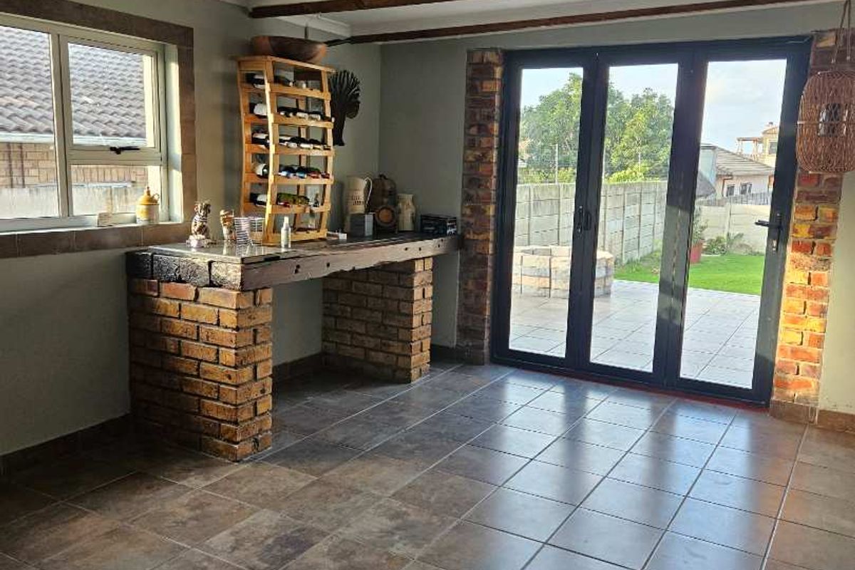 Living area featuring exposed timber ceiling beams, tiled flooring, a built-in brick bar, and aluminium stacker doors opening to the rear garden.