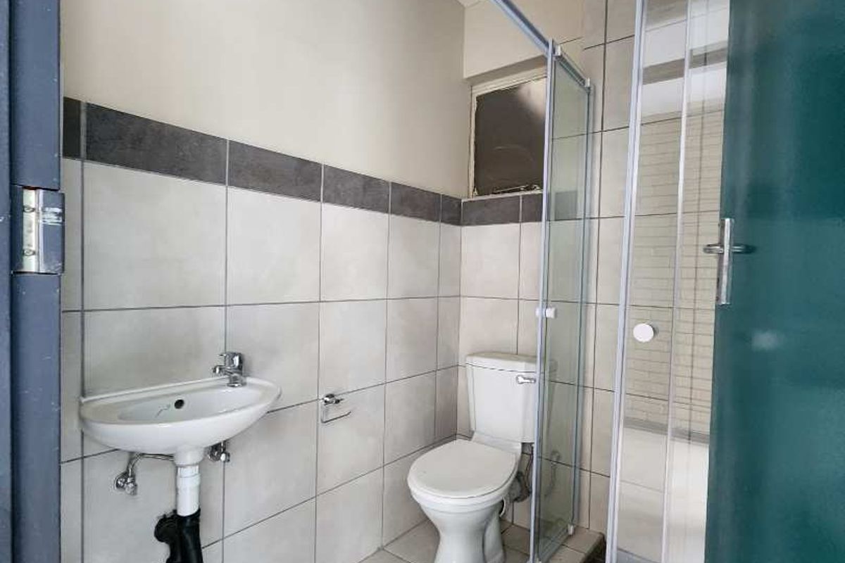 A functional bathroom featuring a wall-mounted basin, toilet, and a glass-enclosed shower with neutral floor and wall tiling.