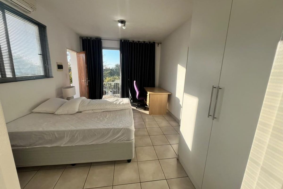 A bedroom featuring tiled flooring, built-in cupboards, and direct access to a balcony through a glass door.