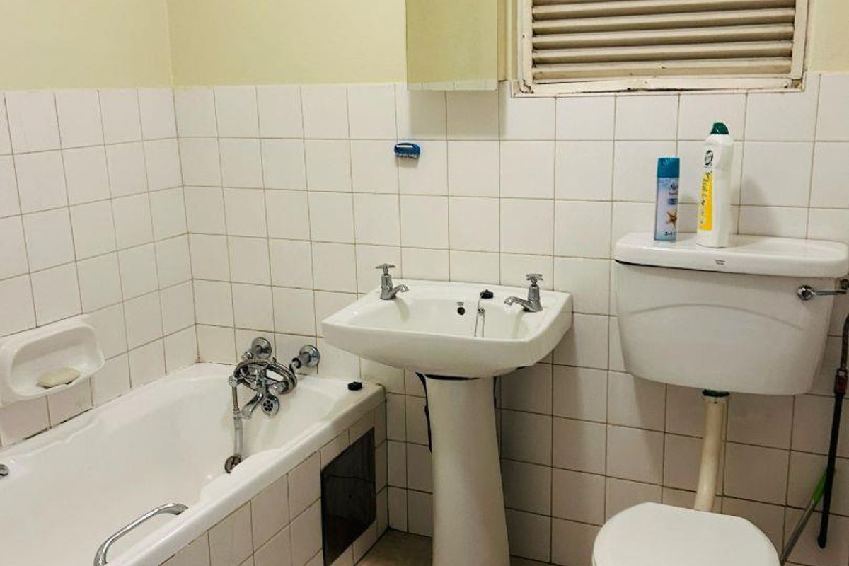 A functional bathroom featuring a pedestal basin, bathtub, and toilet with classic white wall tiling and neutral floor tiles.