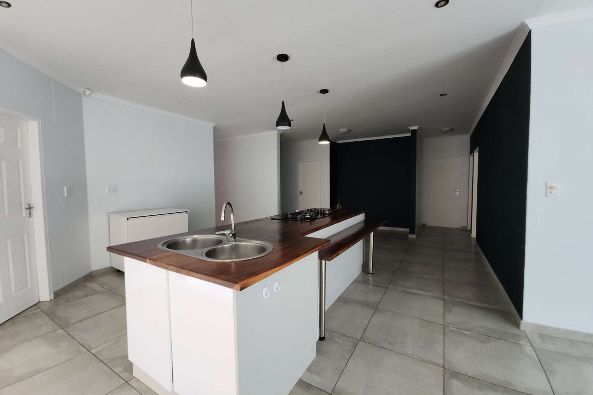 Modern open-plan kitchen featuring a central island with a wooden countertop, integrated sink, and built-in gas hob, complemented by contemporary pendant lighting.