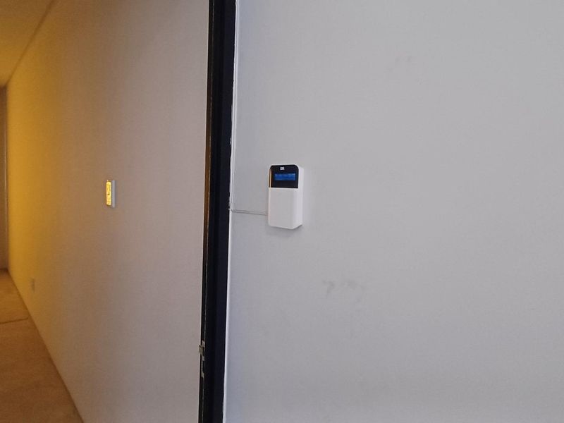 A view of a hallway featuring a wall-mounted alarm system keypad and standard light switch.