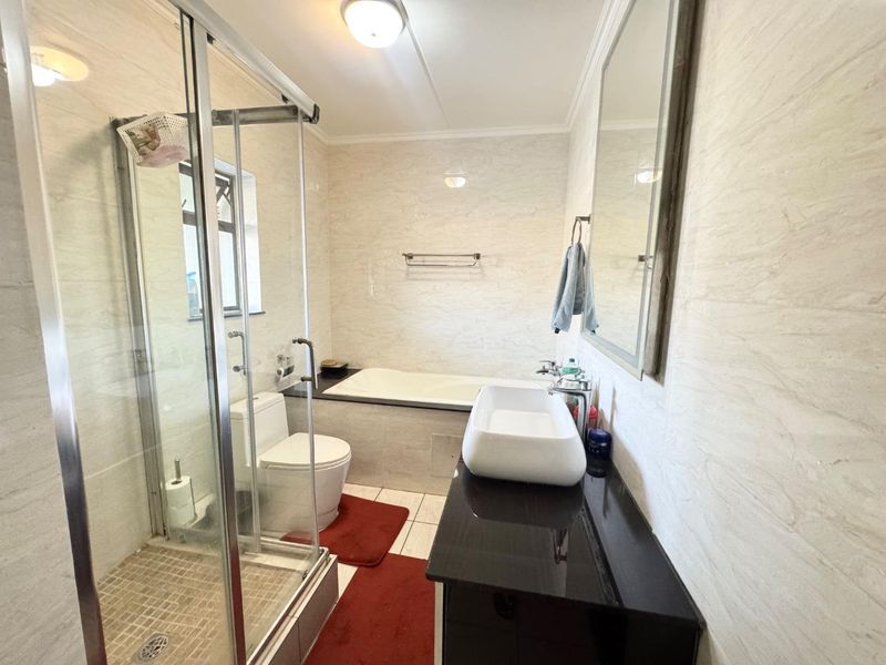 A well-maintained bathroom featuring a glass shower enclosure, a built-in bathtub, a modern vanity basin, and neutral wall tiling.