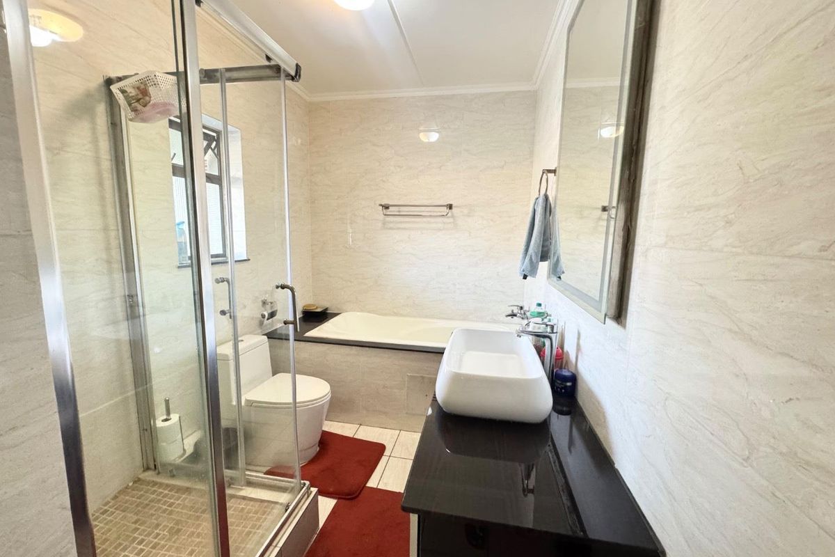 A well-maintained bathroom featuring a glass shower enclosure, a built-in bathtub, a modern vanity basin, and neutral wall tiling.