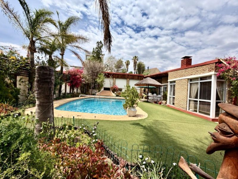 A well-maintained outdoor pool area featuring a swimming pool, artificial lawn, and brick exterior facade with large sliding glass doors.