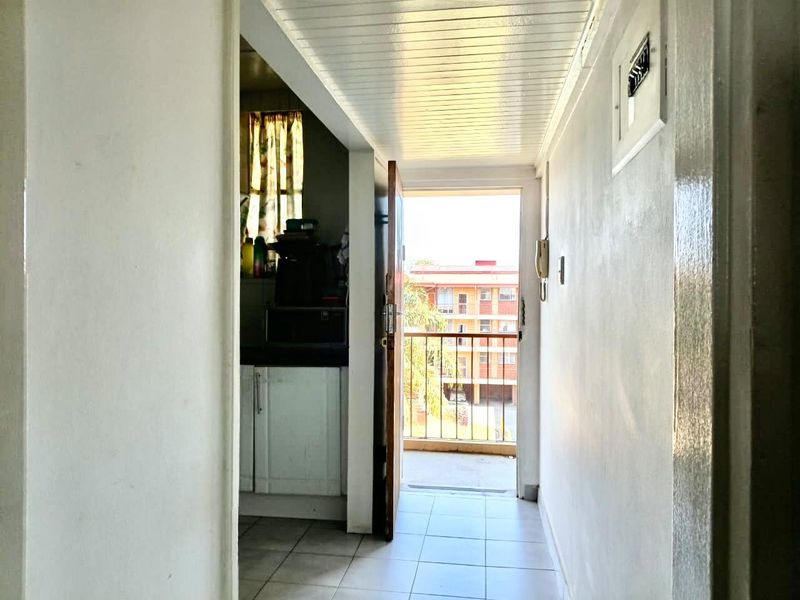 A functional hallway featuring tiled flooring and a tongue and groove ceiling, providing direct access to the kitchen and an outdoor balcony area.