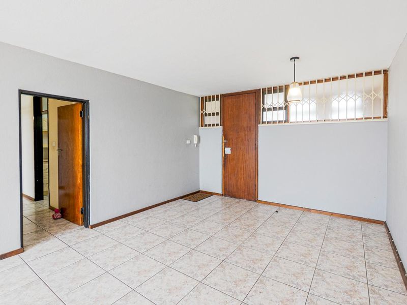 An empty living area featuring neutral tiled flooring, a timber entrance door, and an intercom system, providing a blank canvas for interior design.