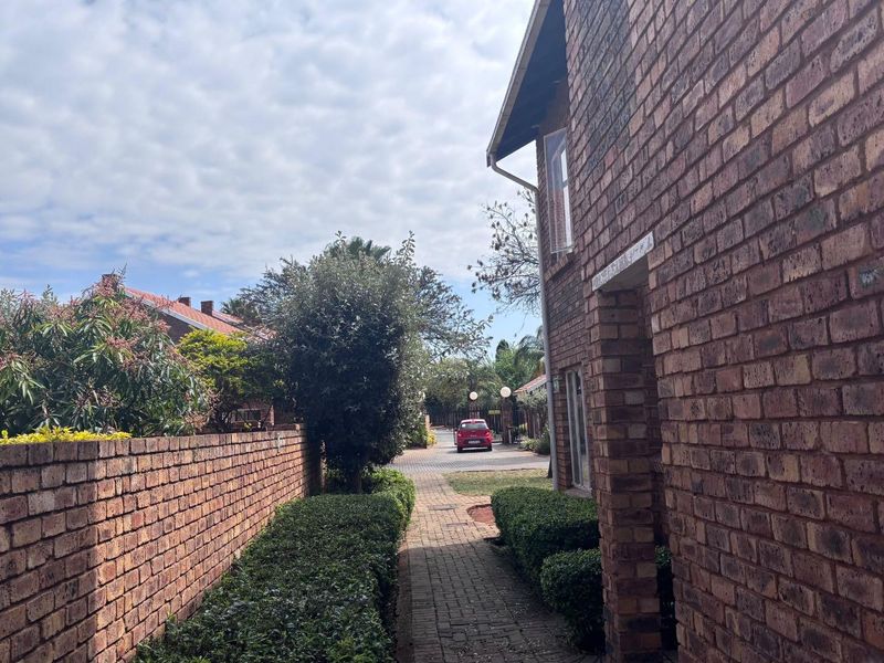 Exterior view of the apartment complex featuring a face brick facade, a paved walkway, and established garden borders.