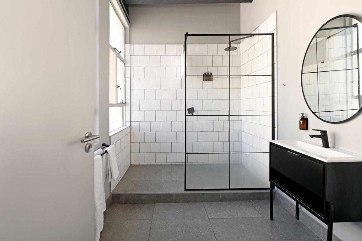 Modern bathroom featuring a walk-in shower with black-framed glass enclosure, white subway tiling, grey floor tiles, and a contemporary vanity unit.