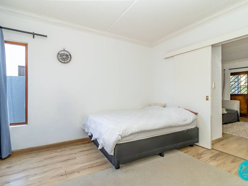 A simple bedroom featuring laminate flooring, a sliding door, and neutral white walls, offering a clean and functional living space.
