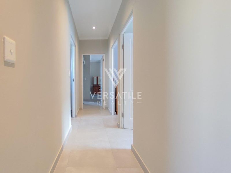 A clean, neutral-toned hallway featuring tiled flooring and recessed downlighting, providing access to multiple rooms within the townhouse.