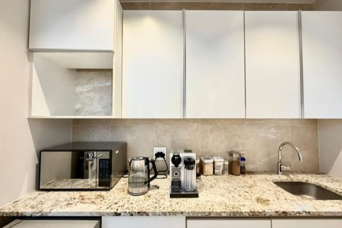 A modern kitchen area featuring white cabinetry, granite countertops, a stainless steel sink, and a tiled backsplash.