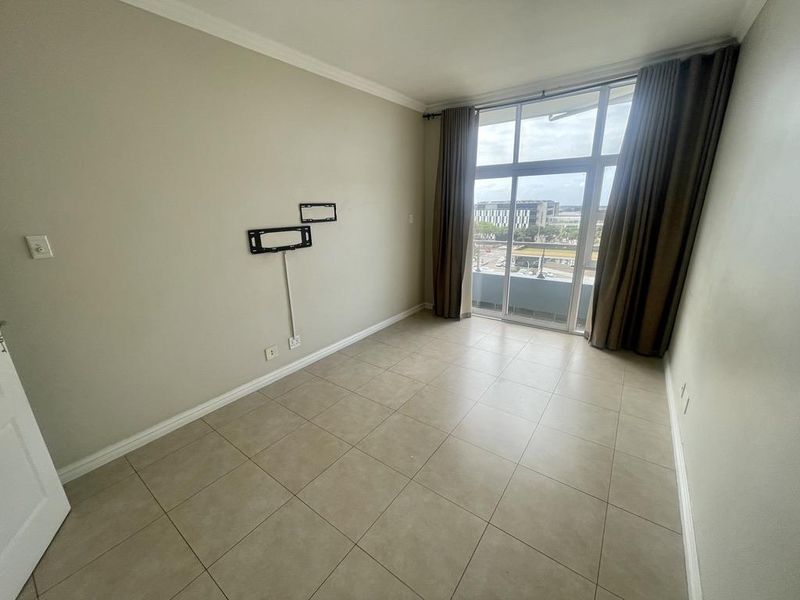An empty bedroom featuring tiled flooring, a wall-mounted TV bracket, and a large sliding glass door providing access to a balcony with city views.