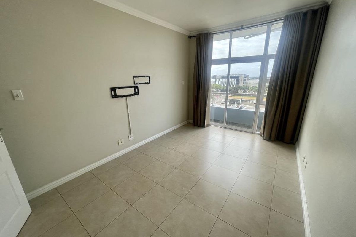 An empty bedroom featuring tiled flooring, a wall-mounted TV bracket, and a large sliding glass door providing access to a balcony with city views.