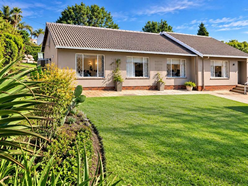 A well-maintained rear exterior view of the house featuring a paved patio area, landscaped garden, and tiled roof.