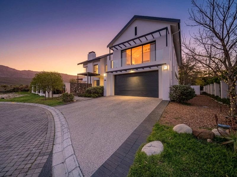 Modern double-story residence featuring a paved driveway, integrated double garage, and an upper-level balcony with glass balustrades at sunset.