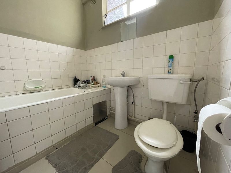 A functional bathroom featuring a pedestal basin, bathtub, and toilet with white wall tiling. The space is dated and would benefit from modernization.