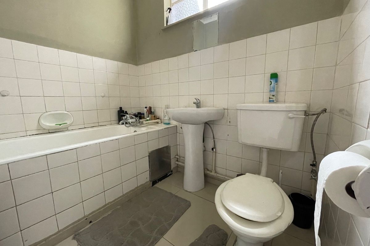 A functional bathroom featuring a pedestal basin, bathtub, and toilet with white wall tiling. The space is dated and would benefit from modernization.