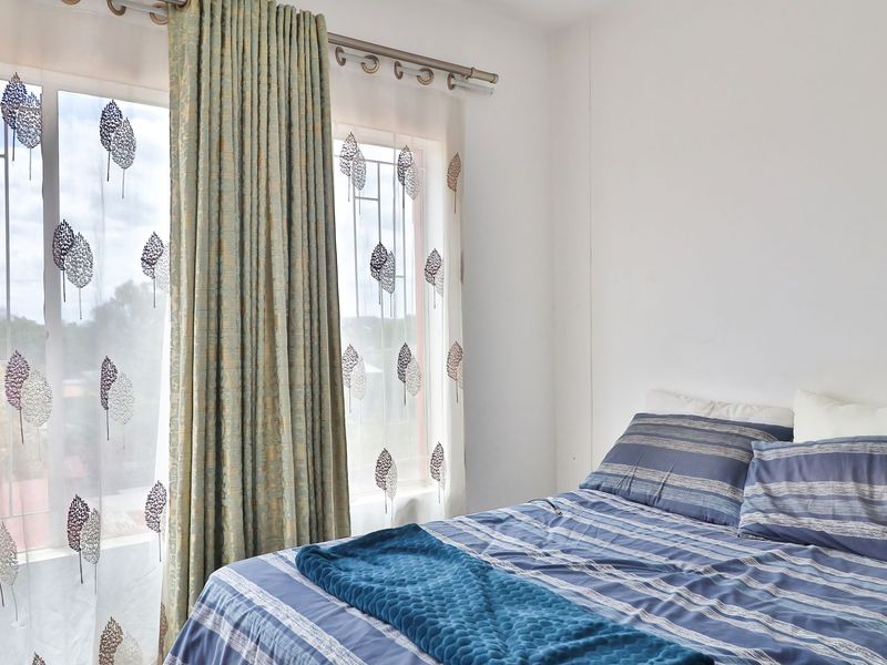 A bright bedroom featuring large windows with security bars and decorative curtains, offering natural light and a view of the surrounding area.