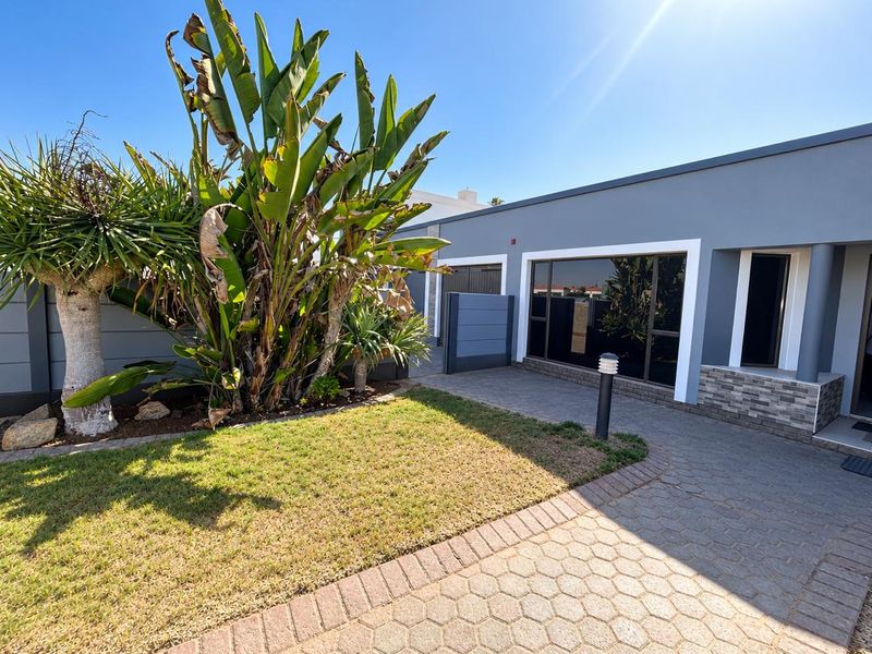 Modern front exterior featuring a paved driveway, stone-clad accents, large windows, and a well-maintained garden area.