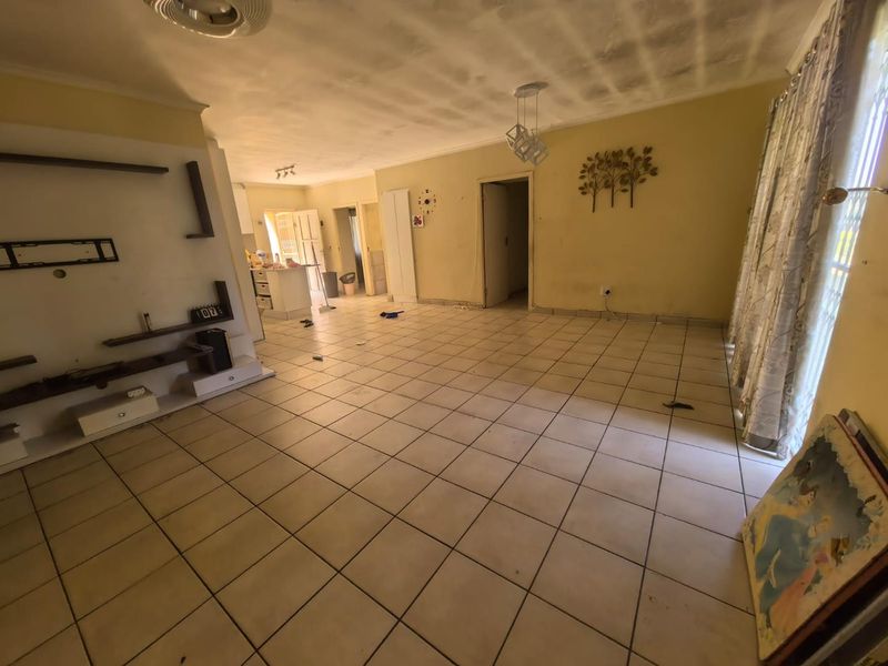 Open-plan living and kitchen area featuring tiled flooring and a built-in media unit, requiring cosmetic updates to the ceiling and walls.